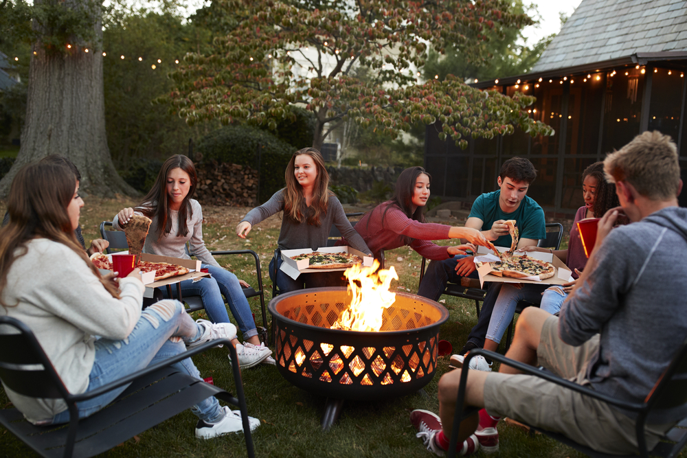 Teenage friends sit around a fireplace eating pizza